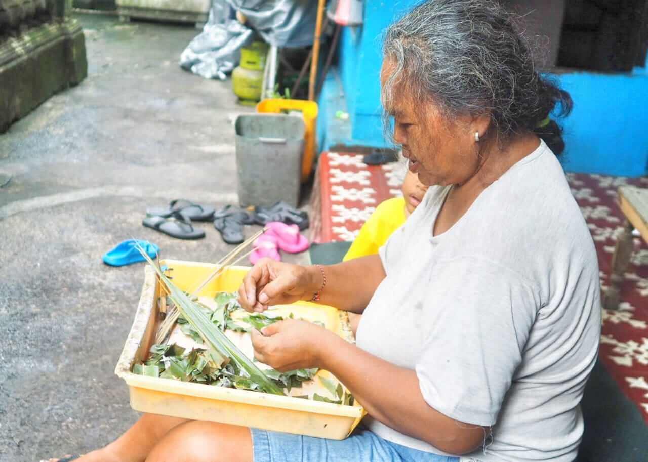 Seorang ibu Bali duduk sambil memilah sayuran segar di halaman rumah.