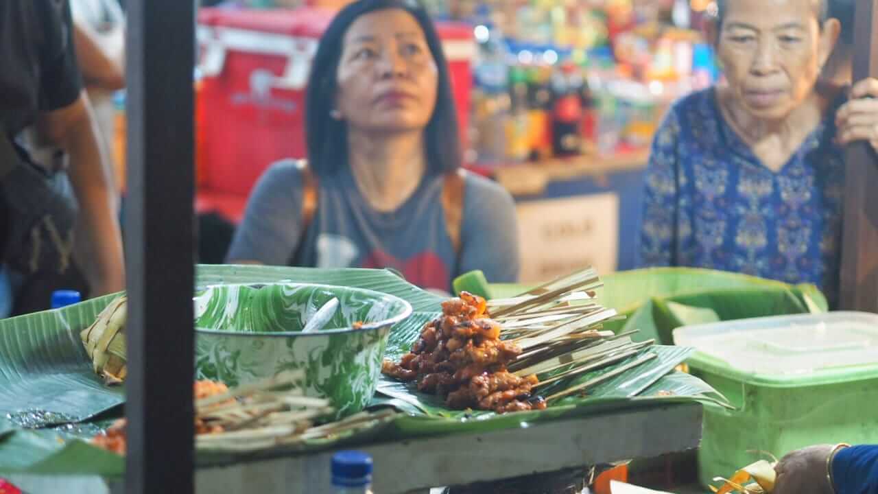 Orang tua menunggu dengan sabar di lapak kuliner malam Pasar Badung untuk menikmati sate khas Bali.
