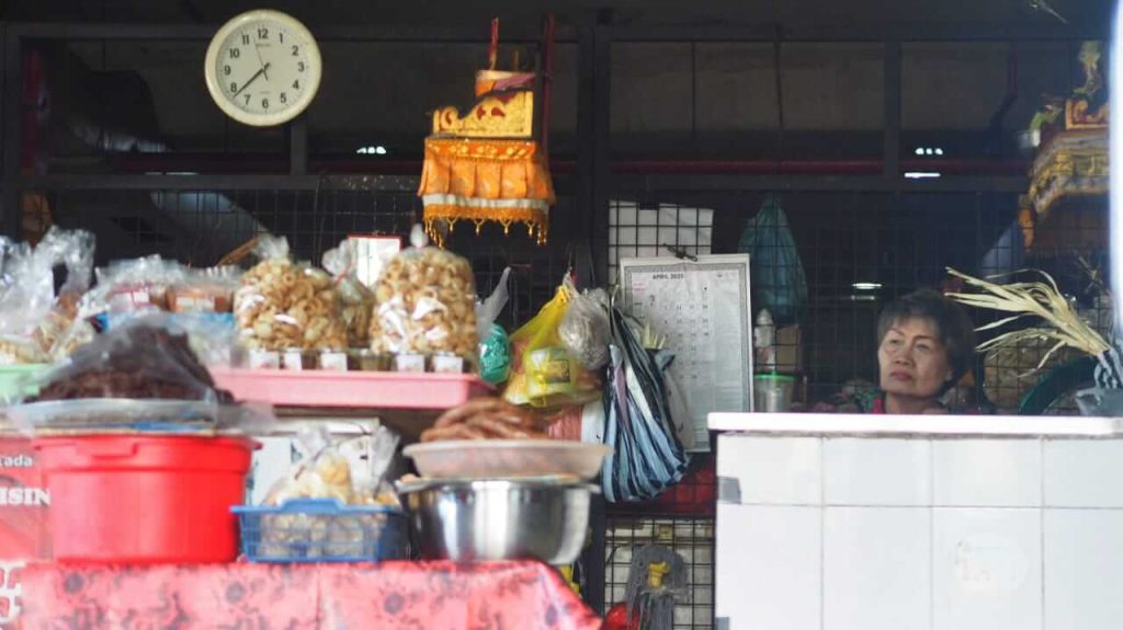 Seorang ibu duduk tenang di depan dagangannya, menatap jauh seolah menghitung hari.