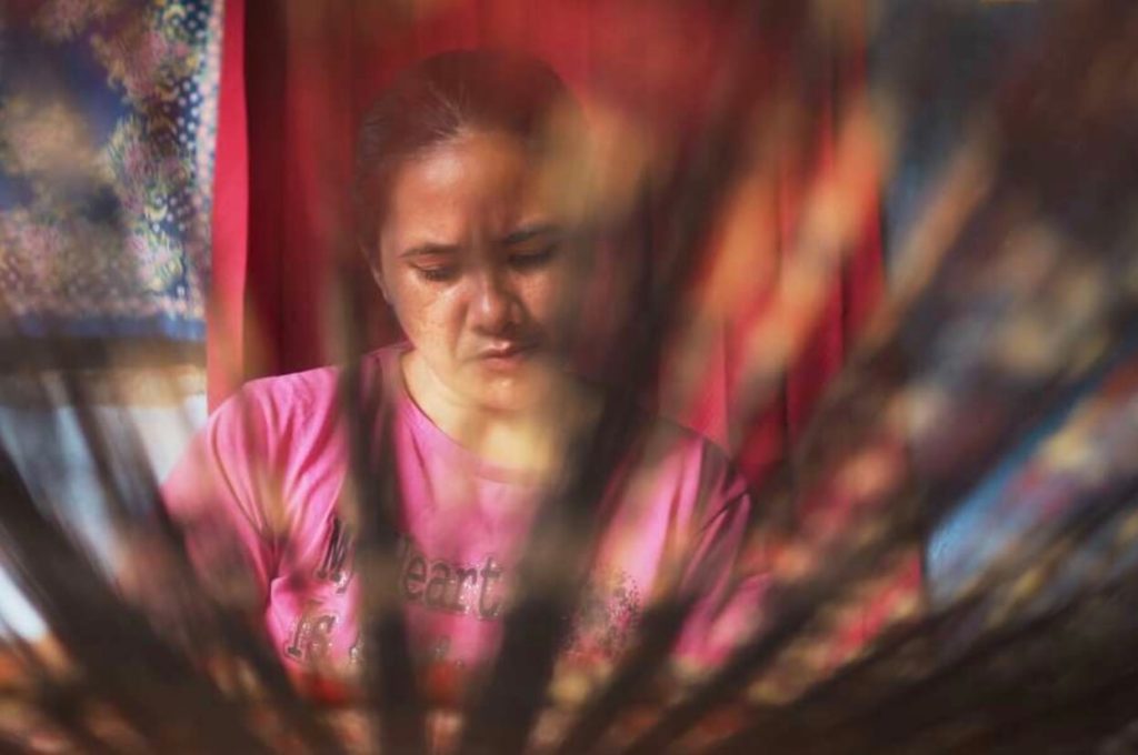 Perempuan Bali dengan penuh ketelitian menenun kain tenun Gringsing, warisan budaya khas dari Desa Tenganan, Bali.