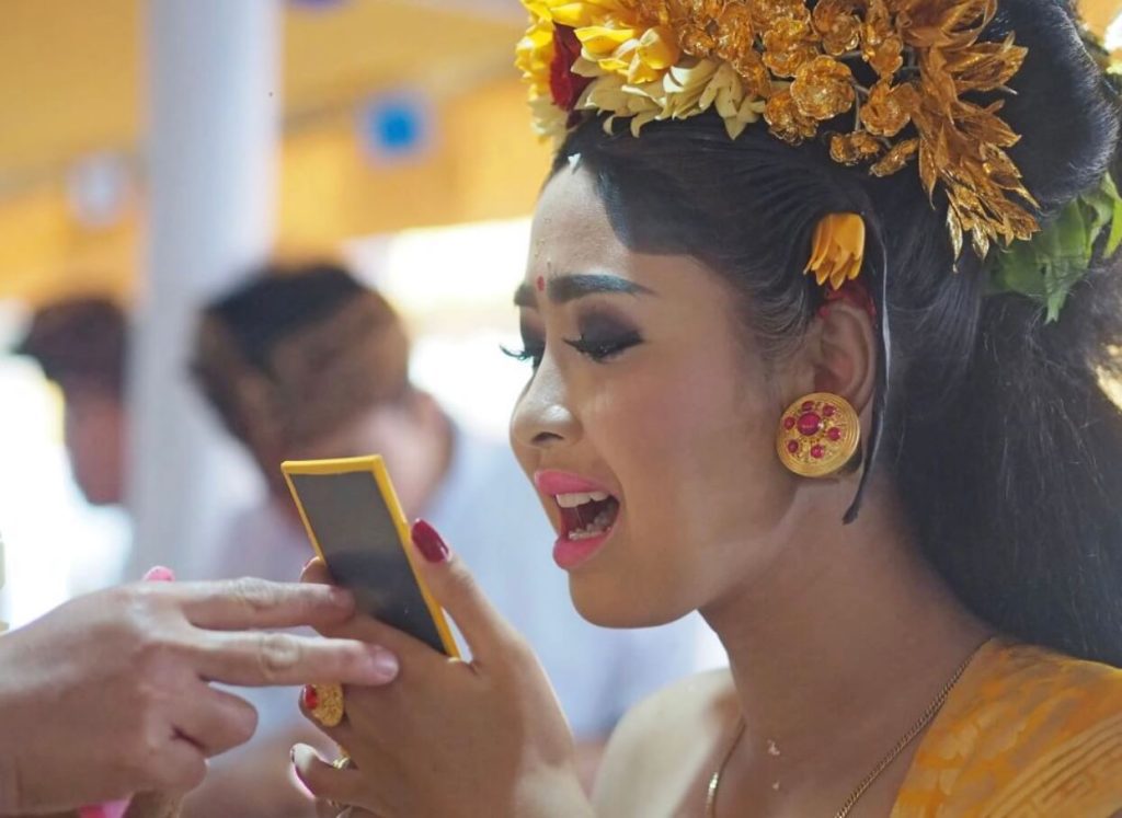 Seorang gadis Bali menjalani upacara potong gigi, duduk anggun mengenakan busana adat lengkap.