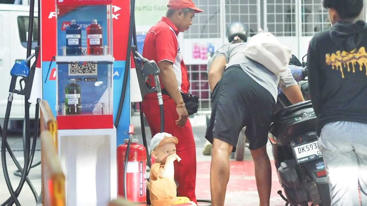 Bule dan anaknya menunggu isi bensin di Bali dengan gaya santai seperti warga lokal.