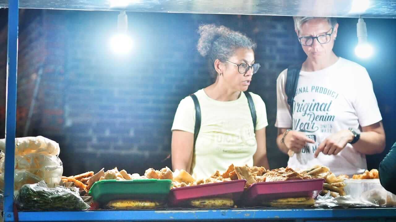 Dua wisatawan asing berbelanja gorengan di pasar malam tradisional Sanur, Bali, menikmati kuliner khas pasar malam yang menggoda selera turis.