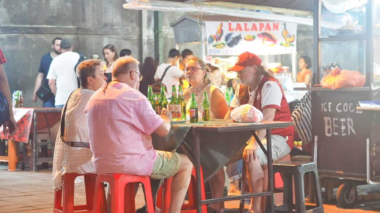 Turis asing menikmati makanan tradisional Bali sambil menikmati segelas bir, sebuah kegiatan populer yang memadukan cita rasa lokal dengan relaksasi.