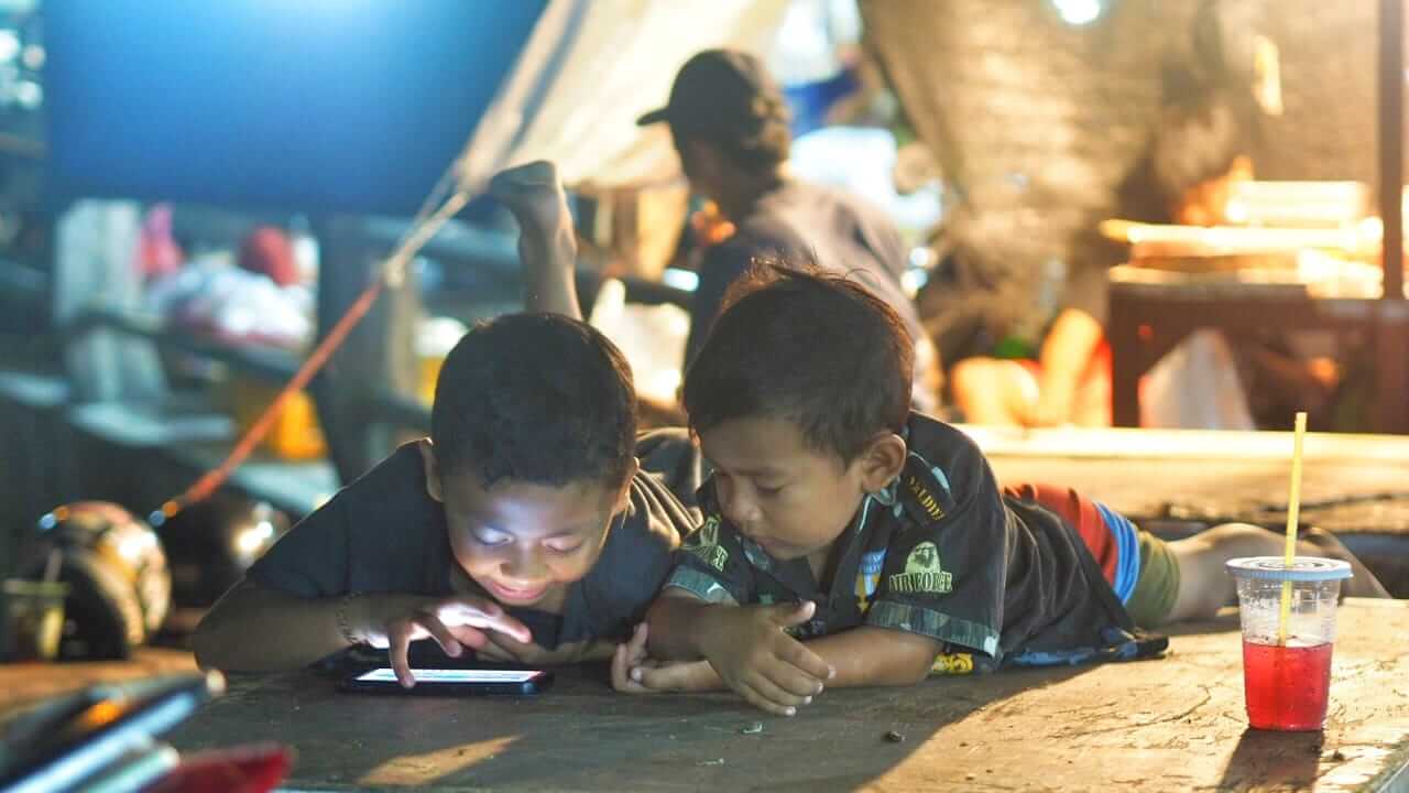 Dua anak bermain gadget bersama di area pasar tradisional.