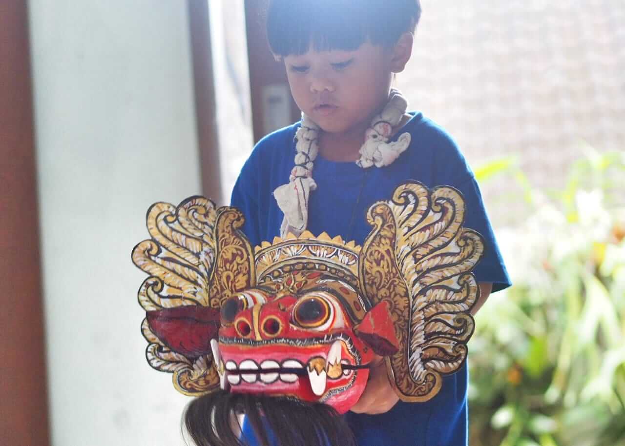 Anak memegang topeng Barong Bali dan menirukan gerakannya dengan semangat.