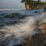 Karang kokoh di Pantai Sawarna dihantam ombak laut, menciptakan pemandangan alam yang dramatis.