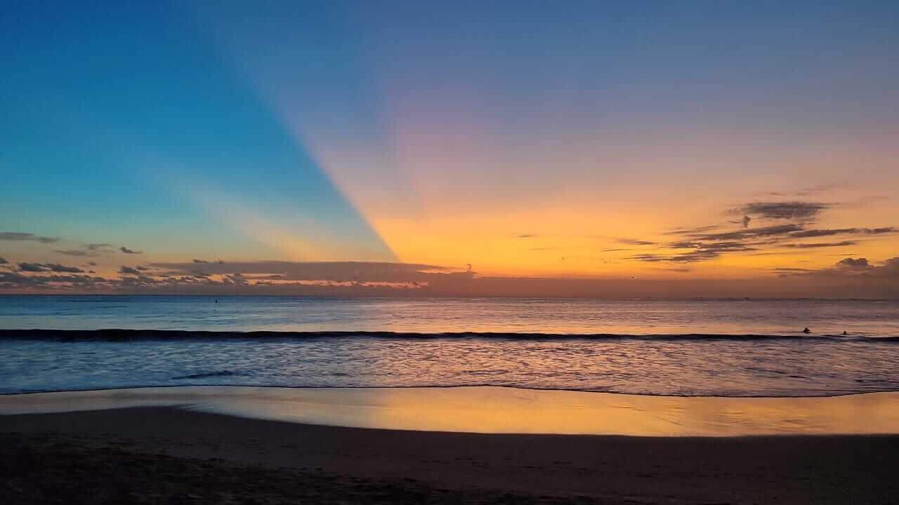 Senja di Jimbaran dengan langit berwarna oranye keemasan saat matahari terbenam di cakrawala.