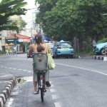 Ibu dan anak bersepeda santai di jalan utama kawasan pesisir Sanur yang tenang dan ramah.