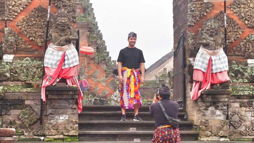 Wisatawan berpose mengenakan kamben di pura sebagai bentuk penghormatan terhadap kesucian tempat suci di Bali.