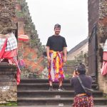 Wisatawan berpose mengenakan kamben di pura sebagai bentuk penghormatan terhadap kesucian tempat suci di Bali.