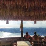 Wisatawan menikmati suasana kafe dengan pemandangan pulau dan pantai dari atas bukit.
