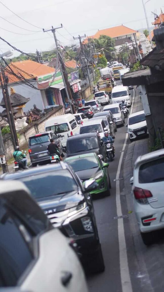 Kemacetan padat merayap dengan deretan kendaraan dan pengendara motor mencari celah di sisi kiri jalan.