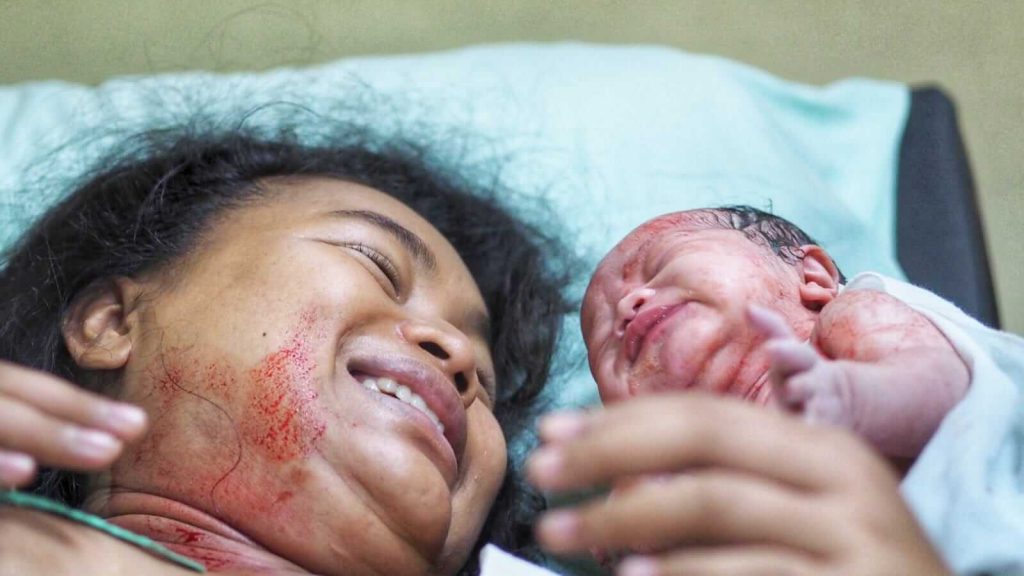 Seorang ibu tersenyum haru menatap bayi yang baru lahir untuk pertama kalinya.