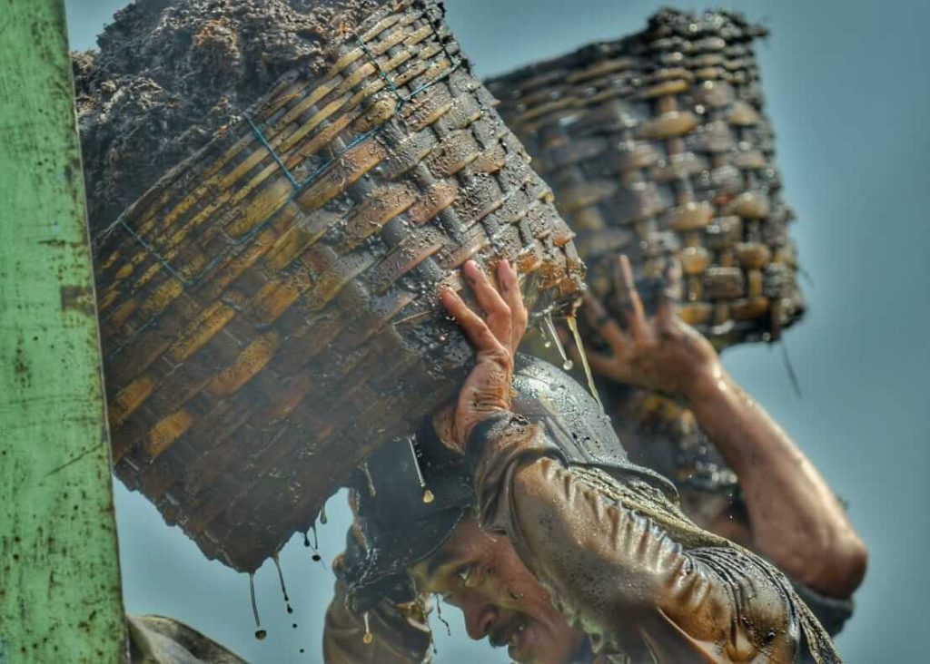 Seorang pria mengangkat beban pasir di atas kepala menggunakan helm sebagai pelindung saat bekerja.