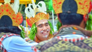 Seorang pria tertawa lepas bersama teman-temannya sebelum tampil menari Tari Bajra saat odalan di pura.