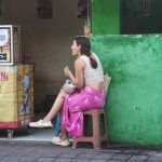 Seorang wisatawan asing duduk santai di pinggir jalan sambil menikmati seporsi martabak.