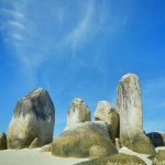 Batu granit besar menjulang di tengah laut dengan hamparan pasir putih dan air jernih.