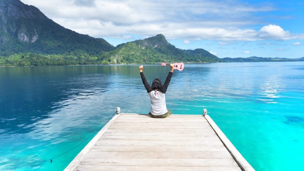 Seorang wanita tersenyum sambil menikmati waktu sendiri di ruang terbuka, memancarkan rasa percaya diri dan kemandirian.