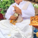 Seorang Ida Pedanda duduk bersila dalam balutan busana adat Bali berwarna putih, memancarkan wibawa dan ketenangan spiritual.