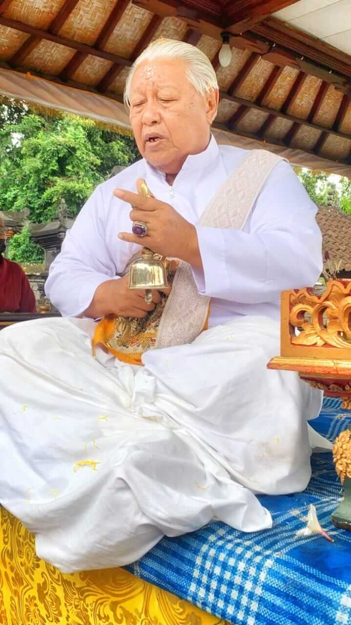 Seorang Ida Pedanda duduk bersila dalam balutan busana adat Bali berwarna putih, memancarkan wibawa dan ketenangan spiritual.