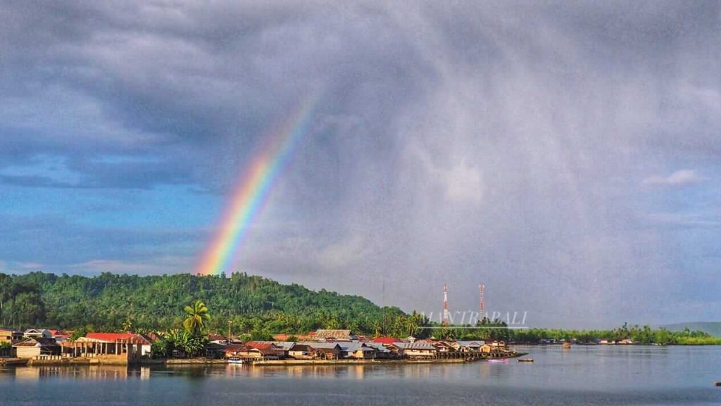 Lengkungan pelangi muncul indah di langit setelah hujan, dengan latar awan kelabu yang perlahan memudar.