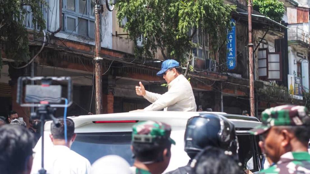 Presiden Prabowo melambaikan tangan menyapa masyarakat dari atas mobil di sekitar pasar.