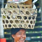 Perempuan Bali berjalan tegap sambil membawa beban di atas kepala.