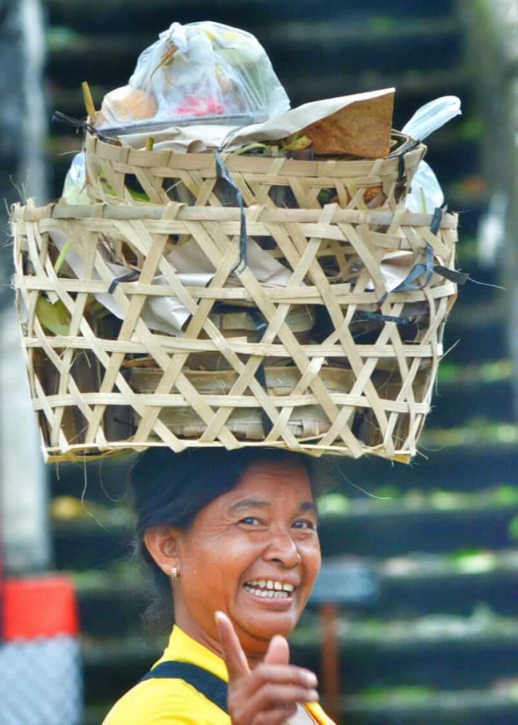 Perempuan Bali berjalan tegap sambil membawa beban di atas kepala.