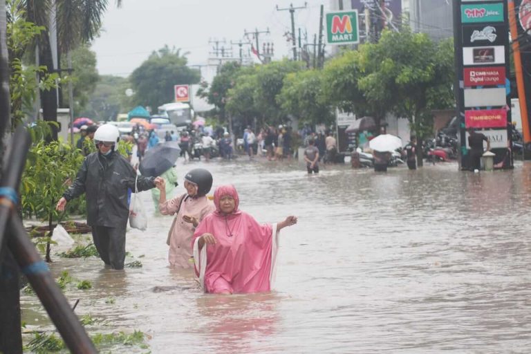 Pejalan kaki melewati jalan yang terendam banjir setinggi paha orang dewasa di Bali.