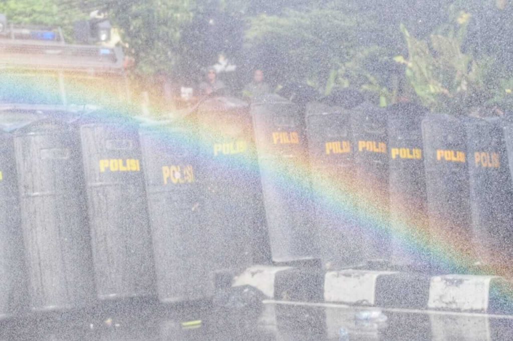 Semprotan water cannon memunculkan pelangi mini di tengah aksi demonstrasi.
