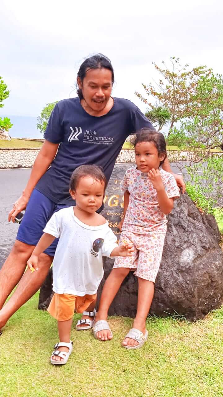 Seorang pria duduk bersama keluarga kecilnya di teras rumah sederhana, memandang sore dengan rasa syukur.