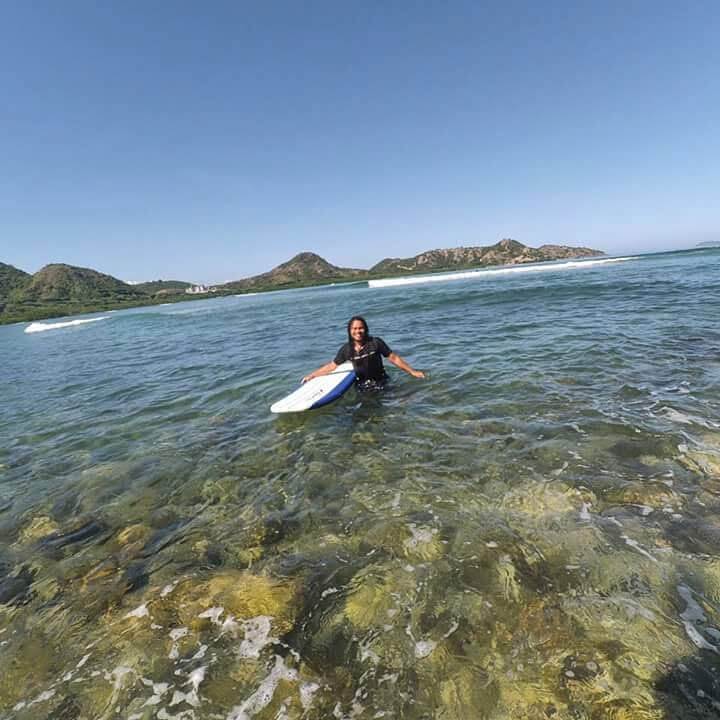 Seorang pemuda berdiri di tepi pantai Sumbawa dengan ombak bergulung di sekitarnya.
