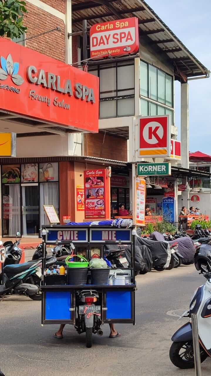 Penjual makanan kaki lima berjualan di tengah keramaian kawasan Seminyak yang dipenuhi kafe dan turis.