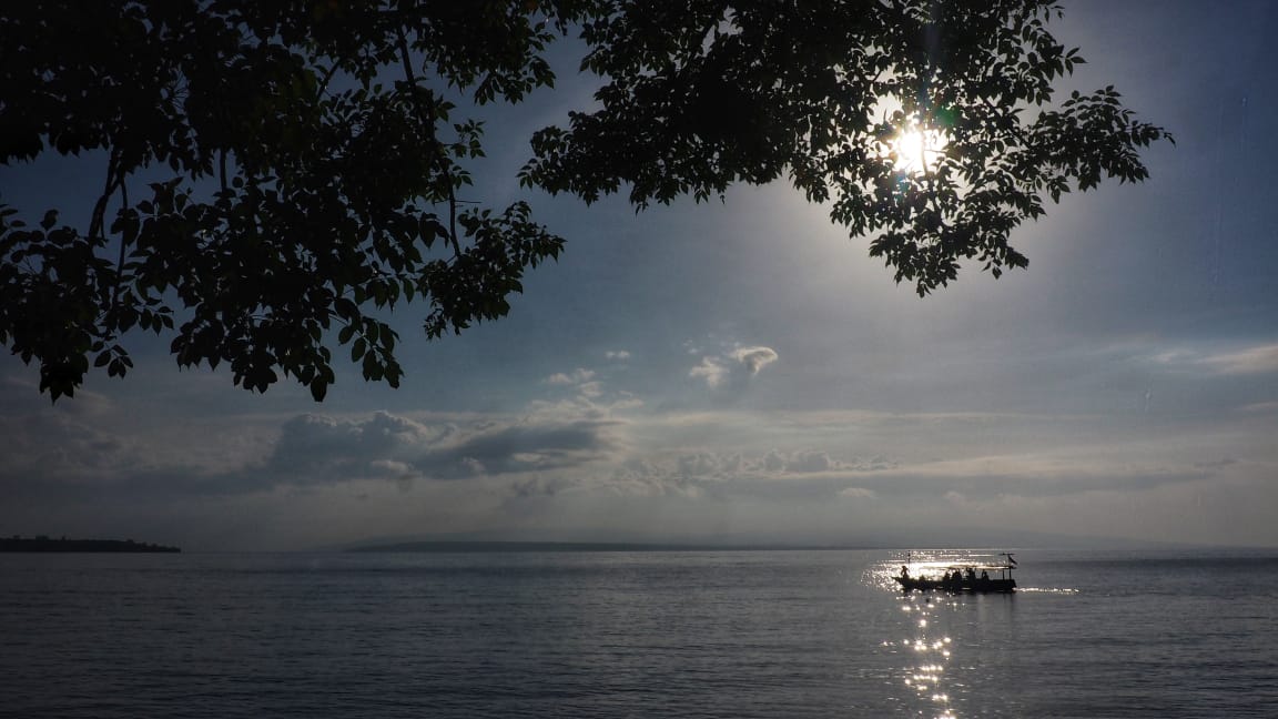Seorang pejalan berhenti sejenak di tepi jalan setapak, menikmati suasana alam yang tenang di bawah cahaya lembut sore hari.
