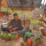 Kakek dan nenek suku Dayak duduk bersama seorang anak muda di pondok kayu, menikmati hidangan tradisional.