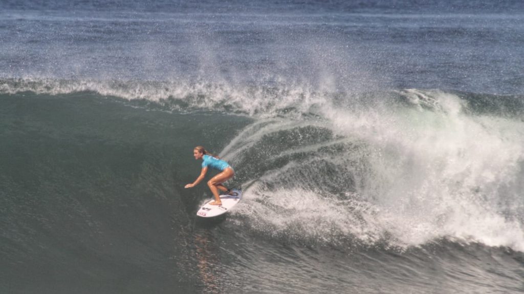 Seorang peselancar menaklukkan ombak dengan penuh keseimbangan dan keberanian di tengah laut.