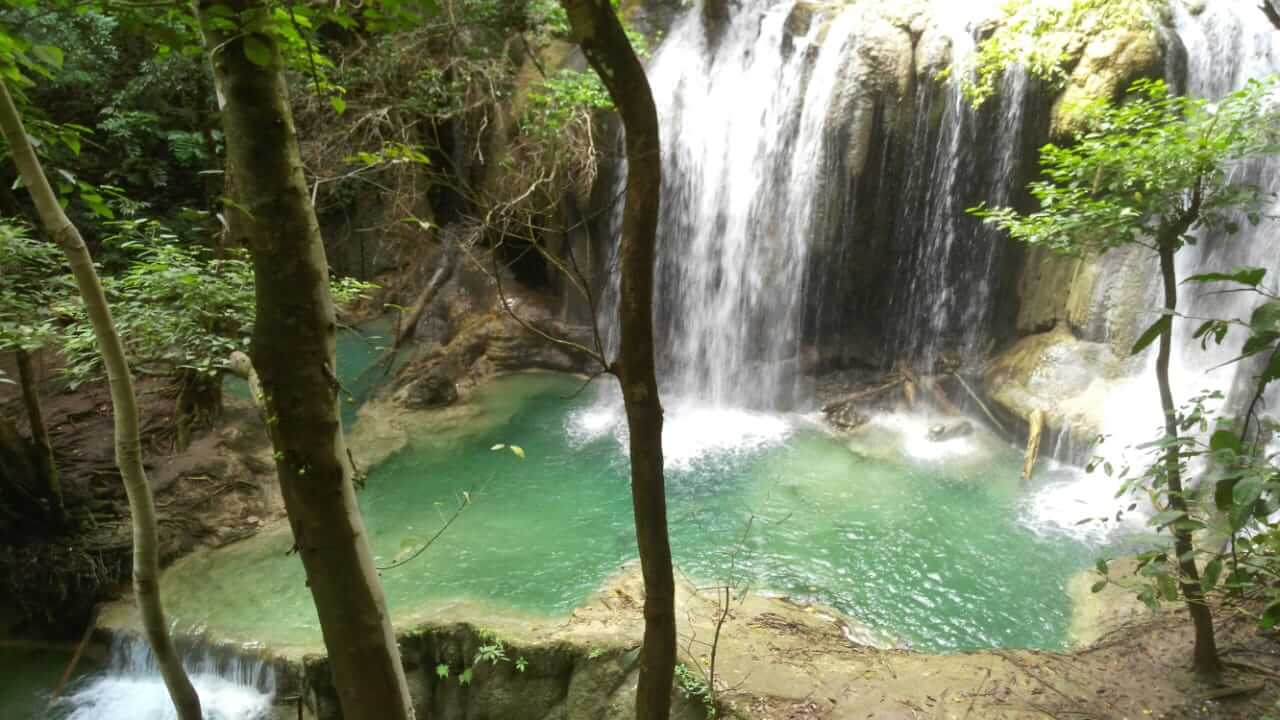 Pemandangan air terjun Mata Jitu di Pulau Moyo dengan aliran air jernih dan pepohonan tropis di sekitarnya.