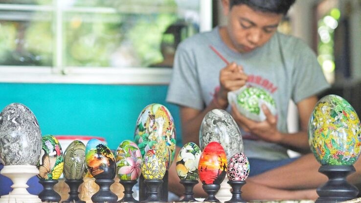 Seorang seniman Bali tengah melukis motif tradisional di atas permukaan telur dengan kuas halus.