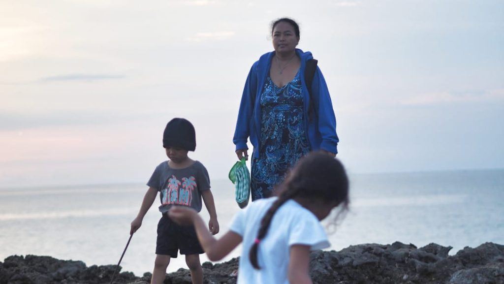 Seorang ibu muda duduk termenung sambil menggendong anaknya, menggambarkan dilema antara peran keluarga dan tuntutan zaman modern.