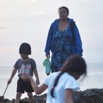 Seorang ibu muda duduk termenung sambil menggendong anaknya, menggambarkan dilema antara peran keluarga dan tuntutan zaman modern.