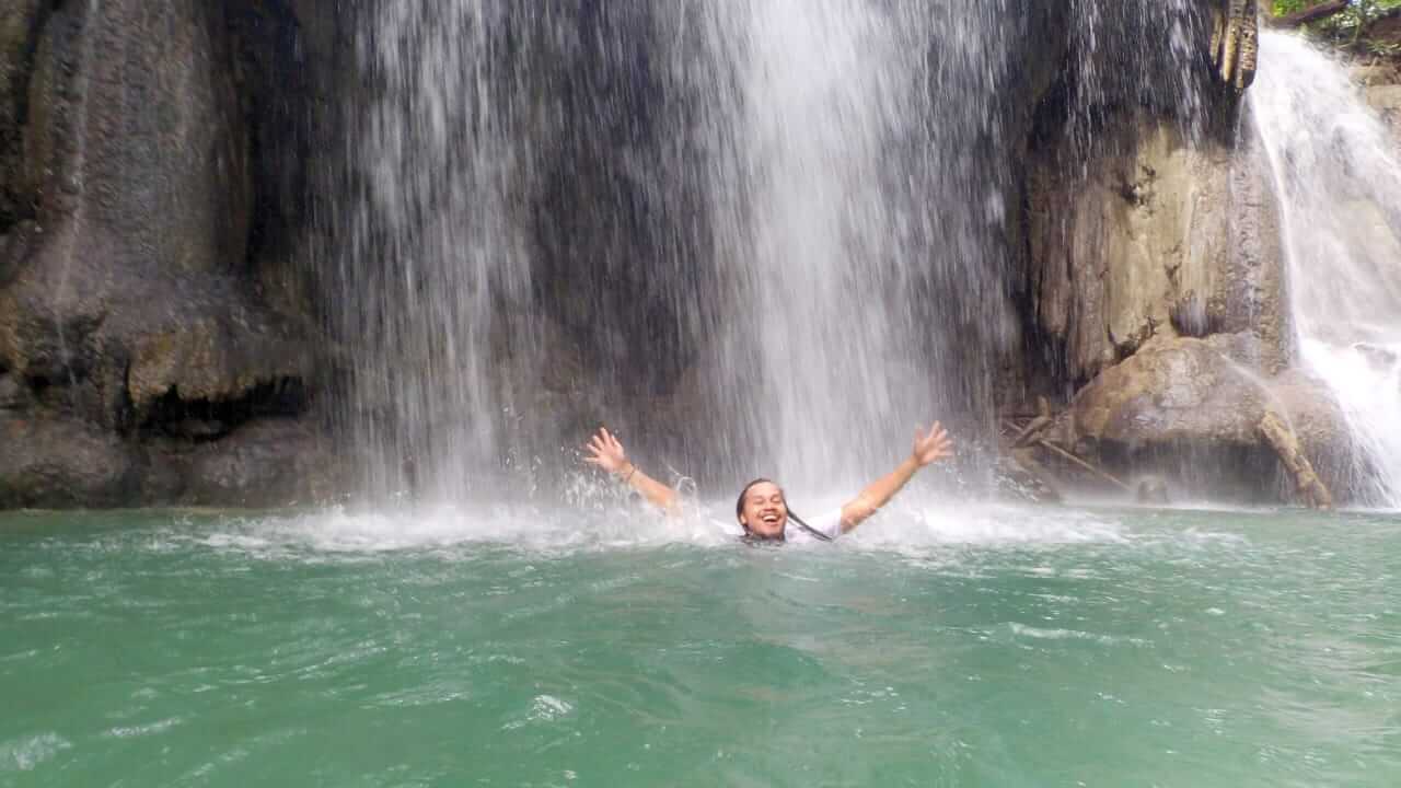 Wisatawan menikmati kesegaran air terjun Mata Jitu di Pulau Moyo, dikelilingi pepohonan hijau yang rimbun.
