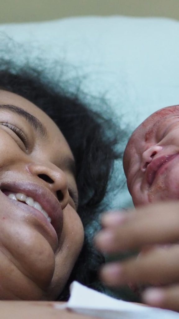 Seorang ibu muda tersenyum haru saat pertama kali memeluk bayinya yang baru lahir.