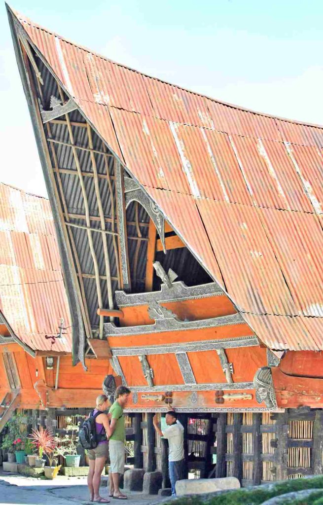 Pemandu lokal menjelaskan makna simbol-simbol pada rumah adat Batak kepada wisatawan.