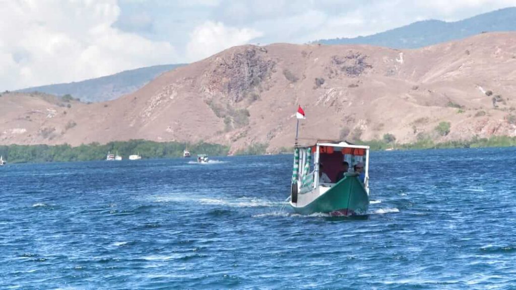 Perahu kecil berlayar di tengah lautan luas dengan latar langit yang tenang, menggambarkan perjalanan hidup manusia.