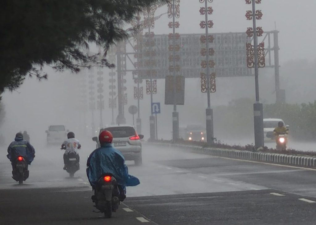Hujan turun di salah satu ruas jalan di Bali, kendaraan melintas dengan hati-hati di tengah kondisi basah.