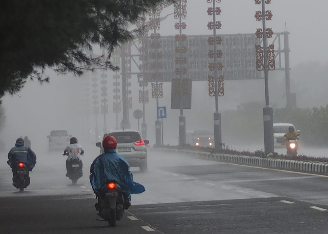 Hujan turun di salah satu ruas jalan di Bali, kendaraan melintas dengan hati-hati di tengah kondisi basah.