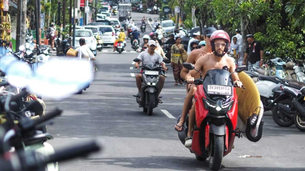 Dua wisatawan asing berboncengan sepeda motor sambil membawa papan selancar, melintasi jalan di kawasan Bali Cliff, Ungasan, Bali.