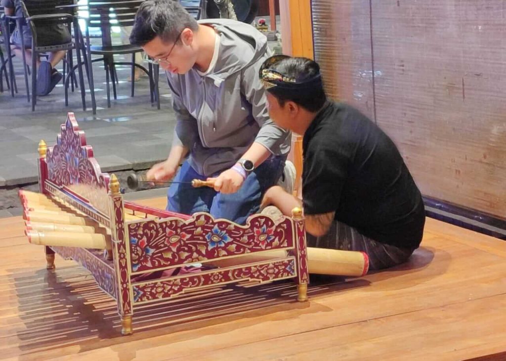 Dua generasi tampak bersama dalam sebuah aktivitas tradisional, menggambarkan proses pewarisan ilmu dan budaya.