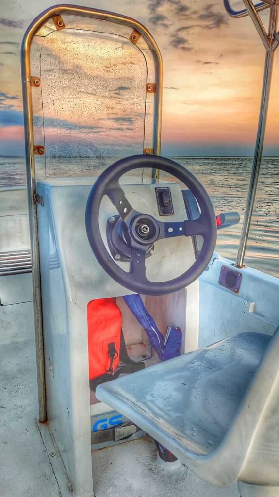 Siluet seorang nahkoda memegang kemudi kapal di tengah laut yang luas, dengan langit senja di belakangnya.